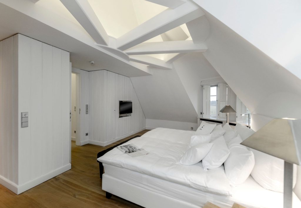 dezent weißes Schlafzimmer in einem Ferienhaus auf Sylt mit einem innovativen Dachstuhl der auch wiederum in weiß ist.