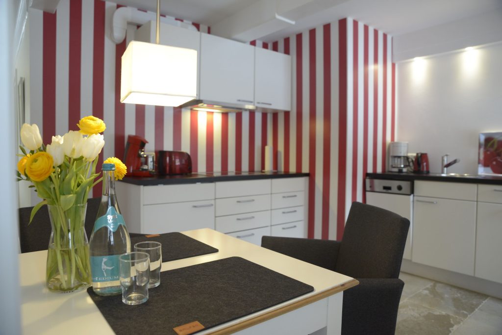 Küchebereich einer Ferienwohnung auf Sylt, mit einer auffällig rot/weiß gestreiften Tapete im Hintergrund.