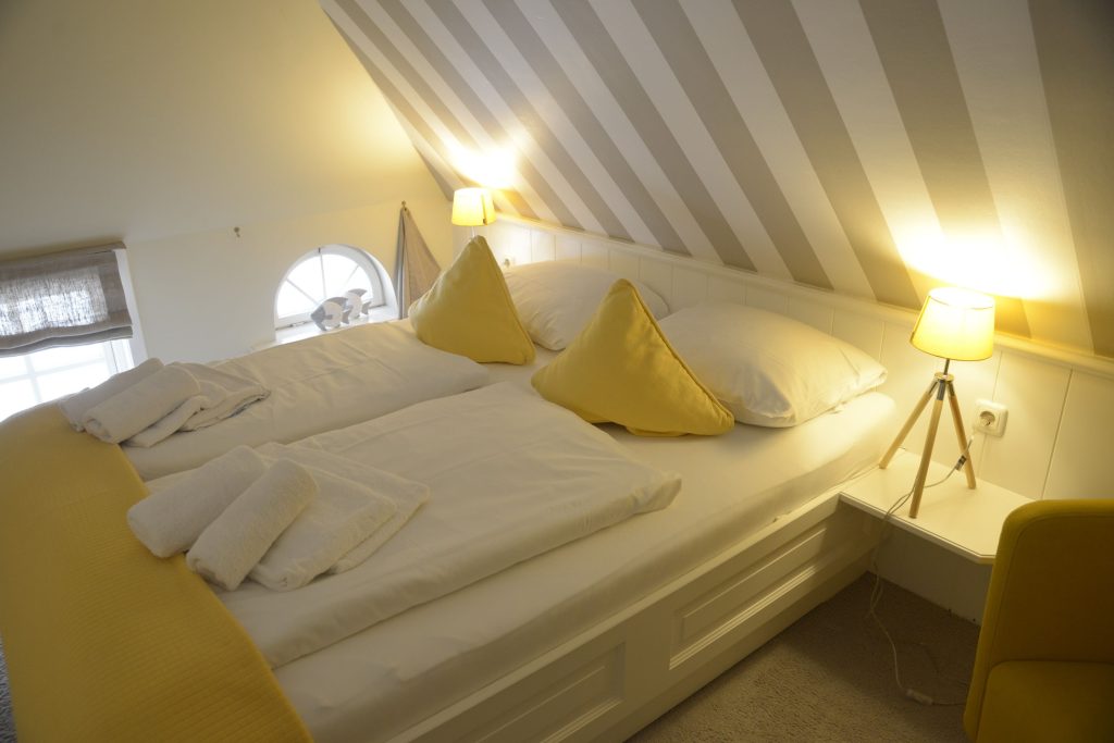 Schlafzimmer mit einer Streifentapete und weiß gelber Bettwäsche in einer Ferienwohnung auf Sylt